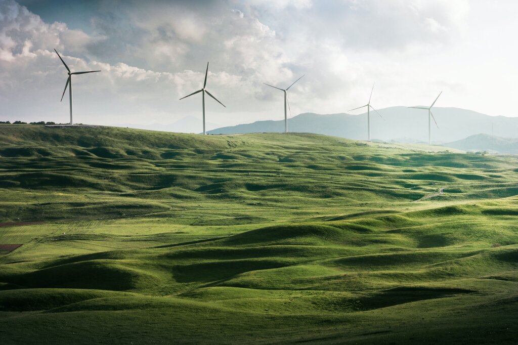 Klimaschutz, Windräder auf einer grünen hügeligen Landschaft.